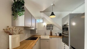 Cocina moderna con armarios blancos, encimera de madera, horno empotrado y una planta colgante.