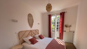 Un dormitorio con cama, mesita de noche, luz en la pared, ventana con cortinas y radiador.