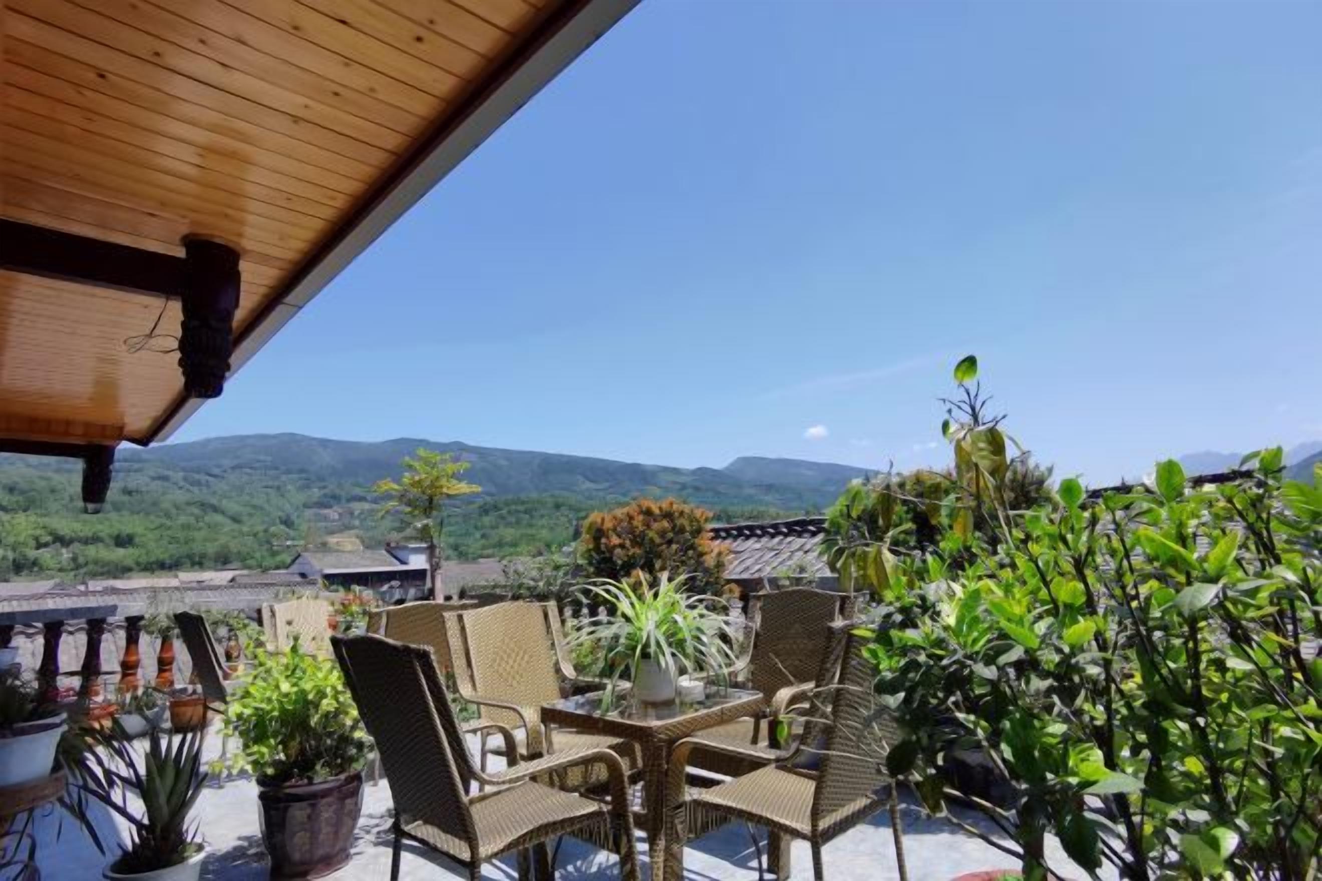 Eine Terrasse mit Korbmöbeln und Topfpflanzen mit Blick auf eine gebirgige Landschaft.