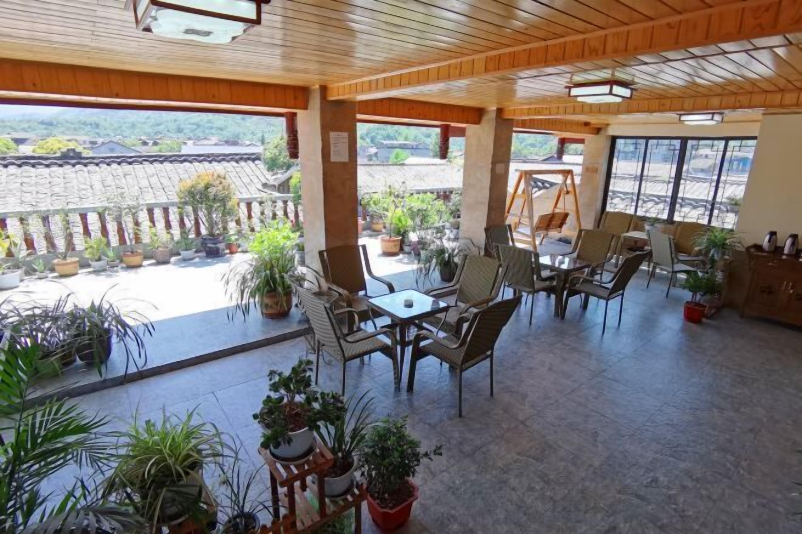 A covered outdoor seating area with tables and chairs, surrounded by potted plants, and overlooking a traditional tiled roof structure.