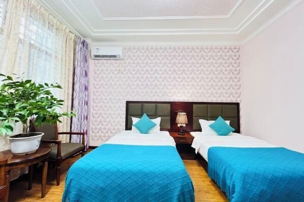 Habitación de hotel con dos camas, una planta en maceta, un escritorio y una ventana con cortinas.