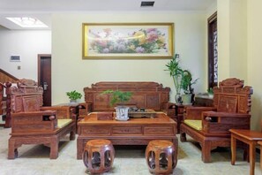 Un ensemble de meubles en bois de style traditionnel comprenant un canapé, deux fauteuils et une table basse, disposés dans un salon orné d’un grand tableau représentant des motifs floraux.