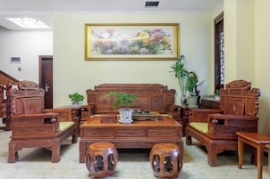 Conjunto de mobiliário de madeira tradicional composto por um sofá, duas poltronas e uma mesa de centro, dispostos numa sala de estar com um grande quadro floral na parede.
