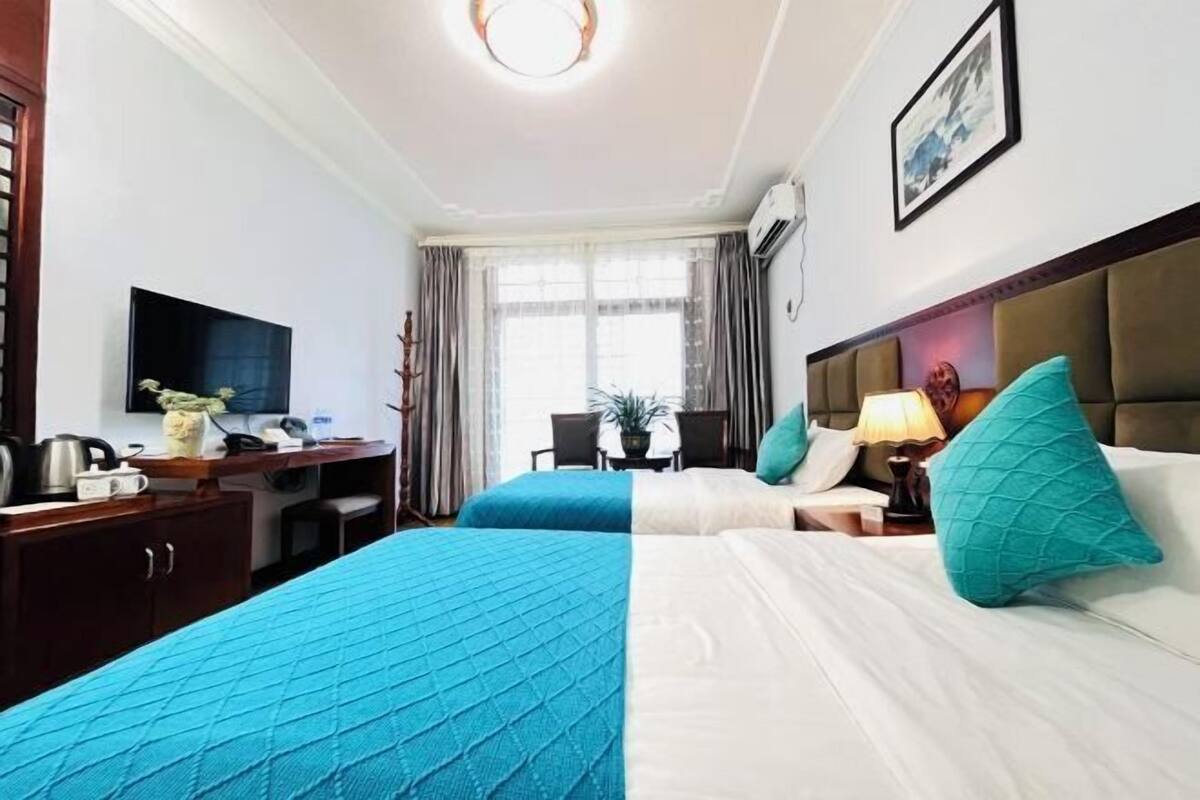 A hotel room with two beds, a desk, a television, and a window with curtains.