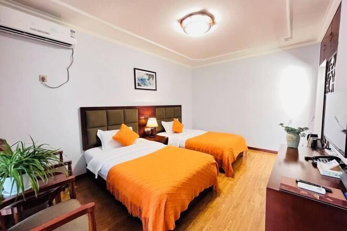 A hotel room with two beds, a desk, a chair, an air conditioning unit, and a framed picture on the wall.