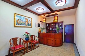 A reception area with a wooden desk, two chairs, a painting, and a door with a decorative pattern.