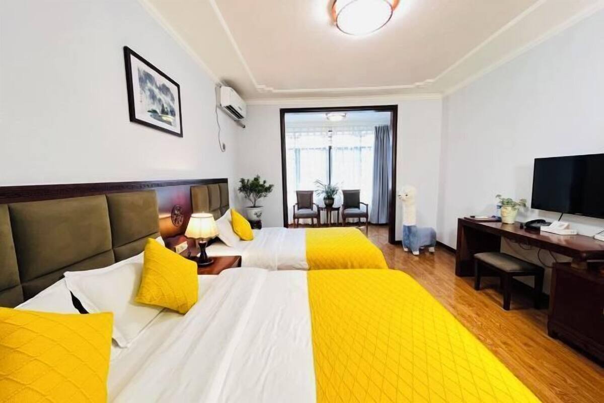 A hotel room with two beds, a desk, a chair, a TV, and a view of the outside.