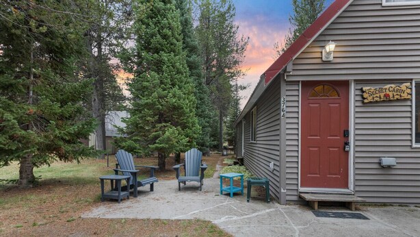 Une cabane avec une porte rouge, deux chaises Adirondack et une petite table à l’extérieur.