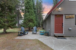 A cabin with a red door, two Adirondack chairs, and a small table outside. - Secret Cabin | Near River, Fire Pit, BBQ 30miles to Yellowstone! (Island Park)