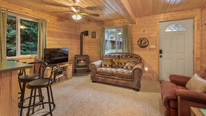 Un intérieur de chalet chaleureux, avec un revêtement mural en bois, une cheminée, un canapé, un téléviseur et un coin bar.