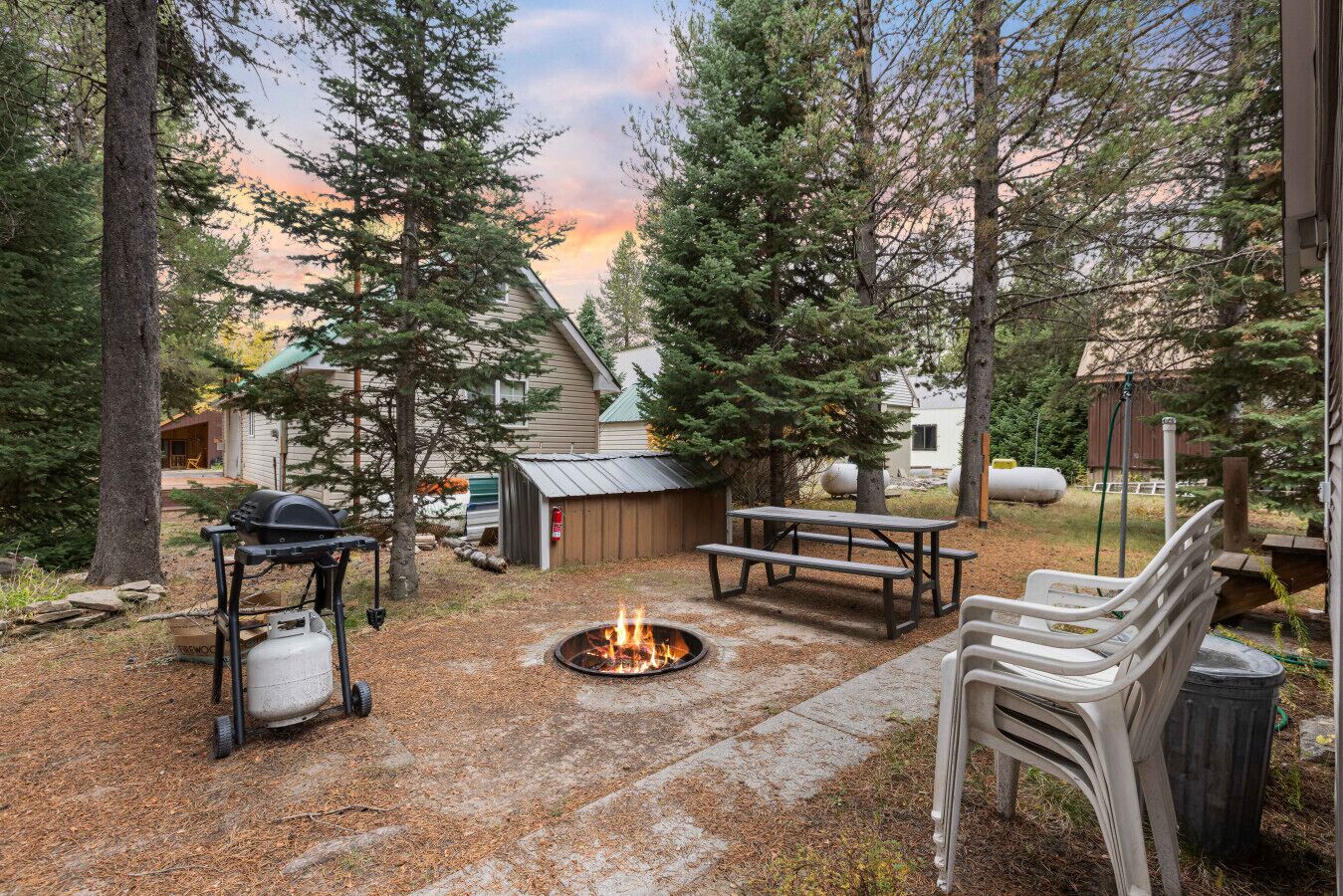 A backyard with a fire pit, picnic table, and grill.