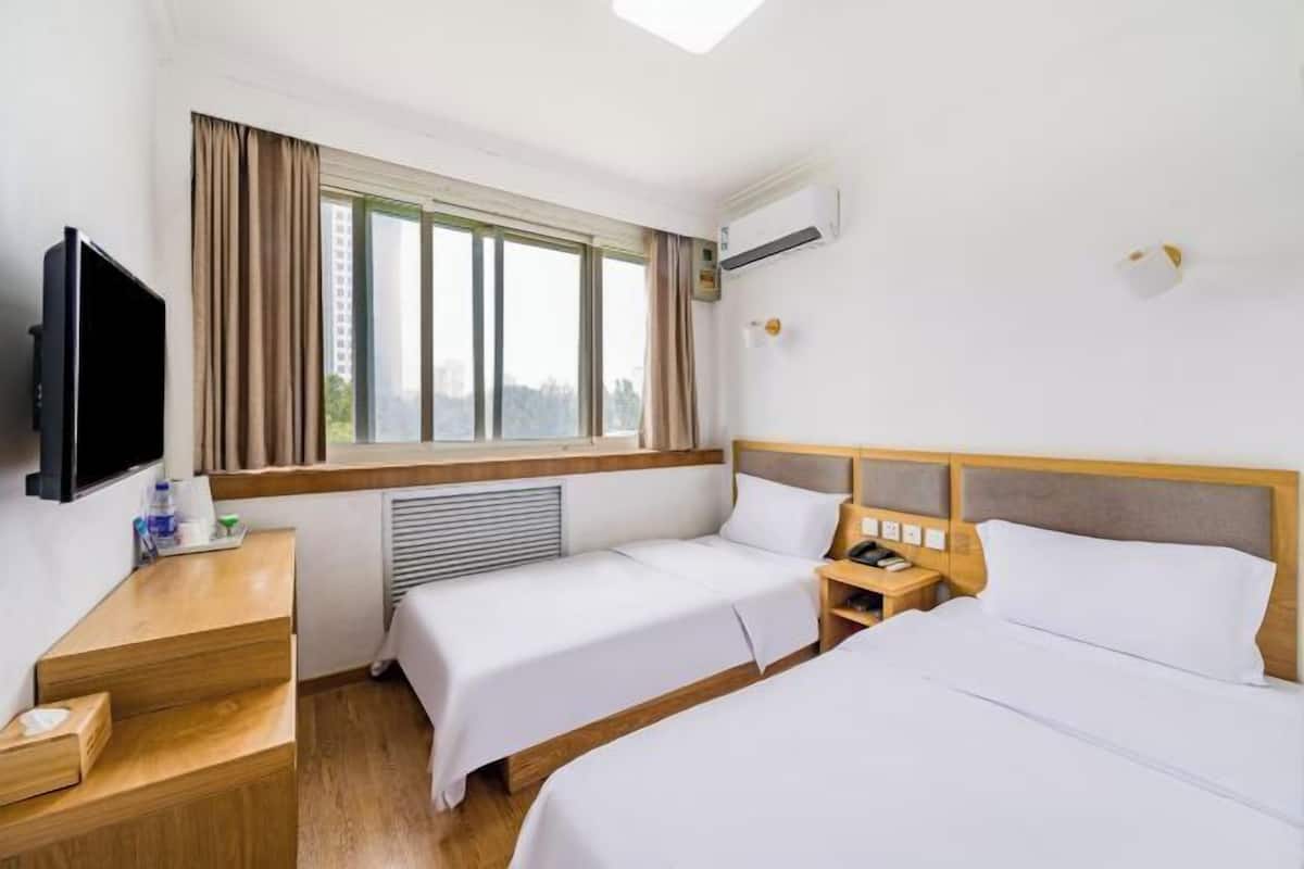 A hotel room with two beds, a TV, a desk with a phone, and a window with curtains.
