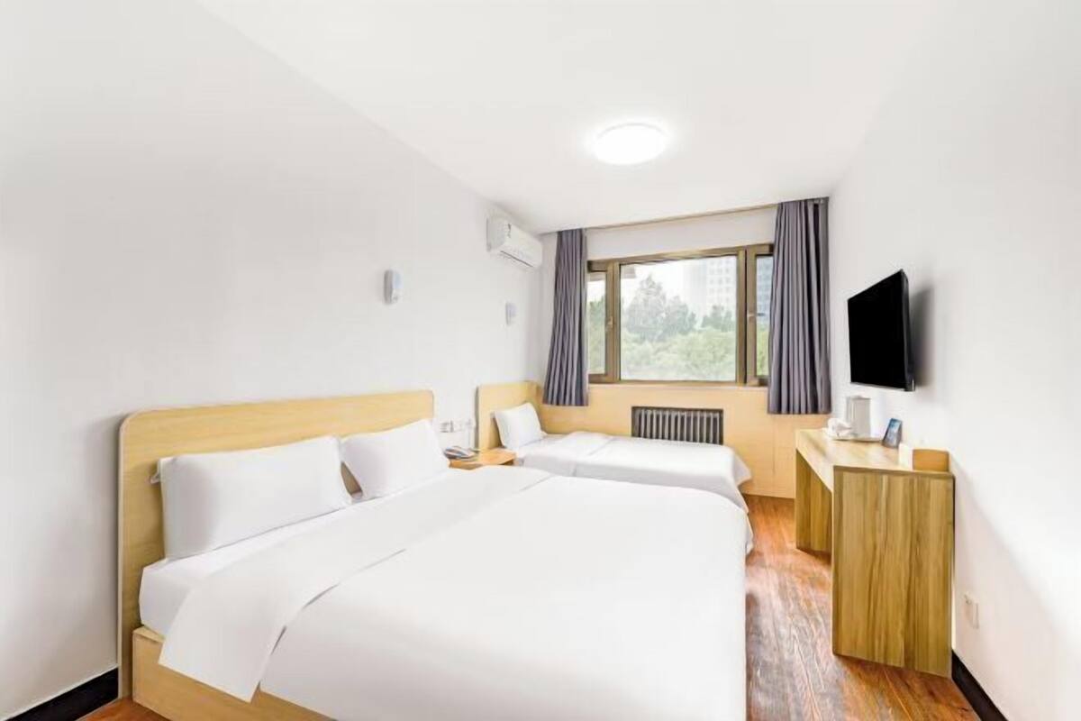 A hotel room with two beds, a desk, a television, and a window with curtains.