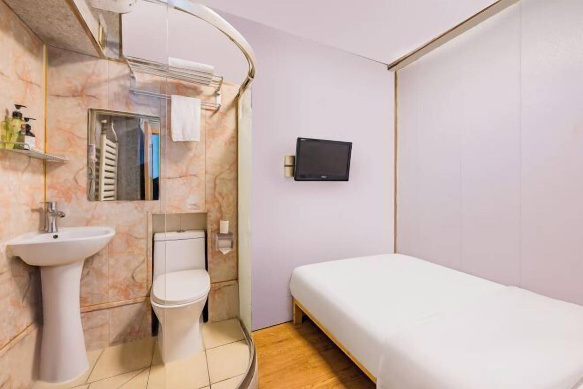 A compact hotel room with a bed, a sink, a toilet, and a TV mounted on the wall.