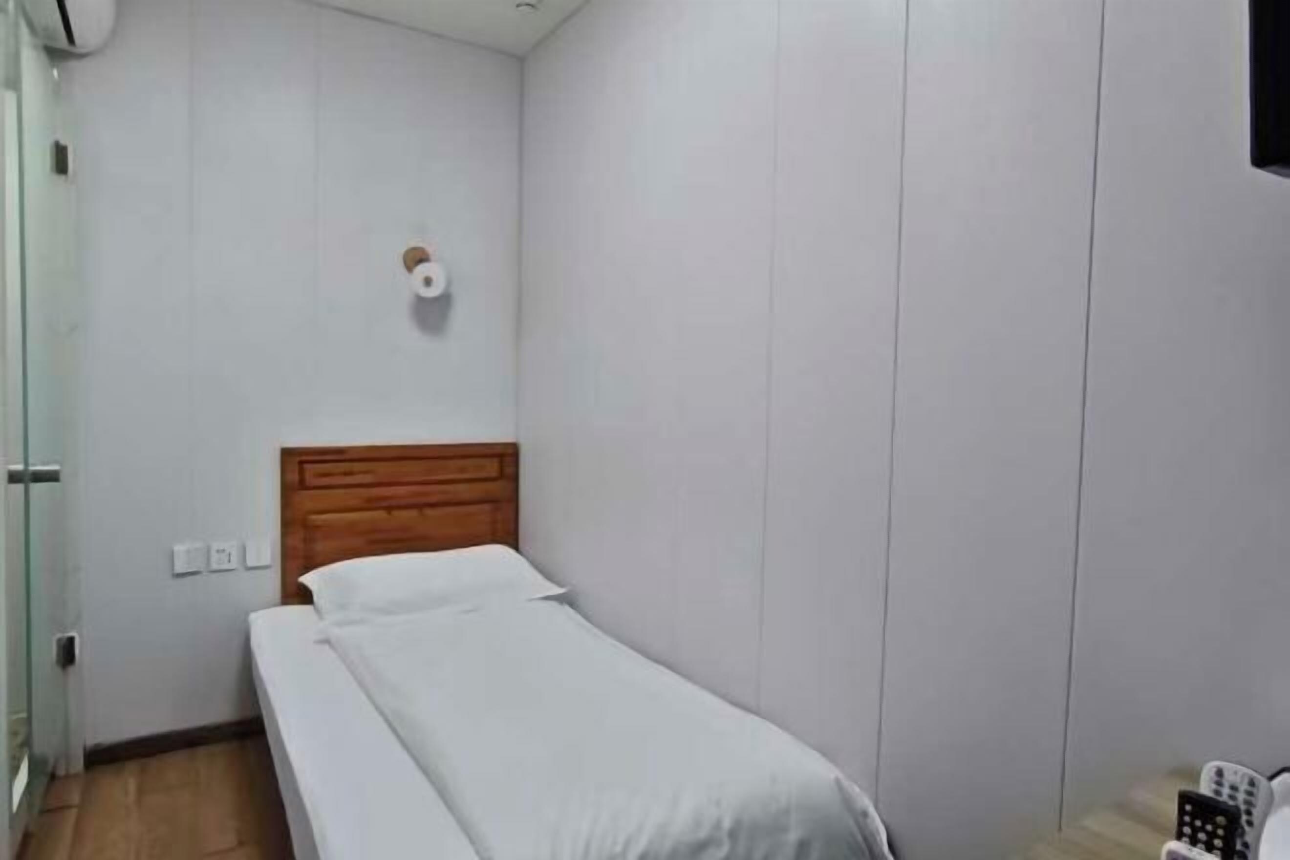 A single bed with a wooden headboard in a room with white walls and a tiled floor.
