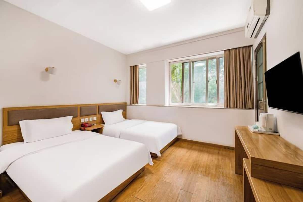 A hotel room with two beds, a wooden desk, a flat-screen TV, and a window with curtains.