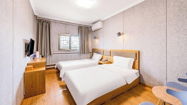 Een hotelkamer met twee bedden, een bureau, een stoel, een televisie en een raam met gordijnen.