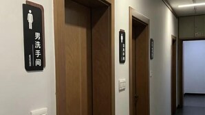 Een gang met houten deuren en borden die de herentoilet en damestoilet aangeven.