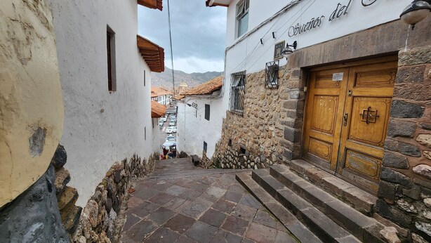 Ένας στενός δρόμος με πέτρινα κτίρια, μια ξύλινη πόρτα και μια πινακίδα που γράφει «Sueno del Jinco».