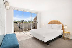 Relax in a spacious room with a large bed, round table, and comfortable sofa, offering a view of the city skyline from the balcony.