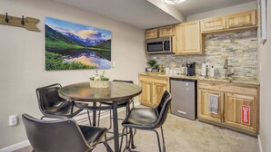 A kitchen with wooden cabinets, a microwave, a dishwasher, and a dining area with a round table and chairs. - Mountain Studio! Cozy Escape with Stunning Views (Cascade-Chipita Park)