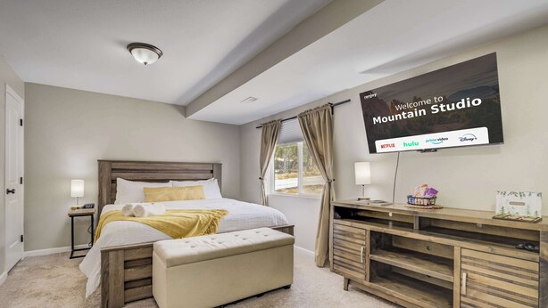 A bedroom with a bed, bedside tables, a TV displaying a welcome message, and a desk with a computer. - Mountain Studio! Cozy Escape with Stunning Views (Cascade-Chipita Park)