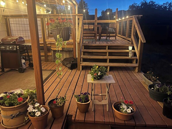 A wooden deck with potted plants, a grill, and a staircase leading to an upper level.