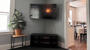 Un soggiorno con una TV a schermo piatto montata al muro, una pianta in vaso, un tavolino di legno e un mobile TV nero.