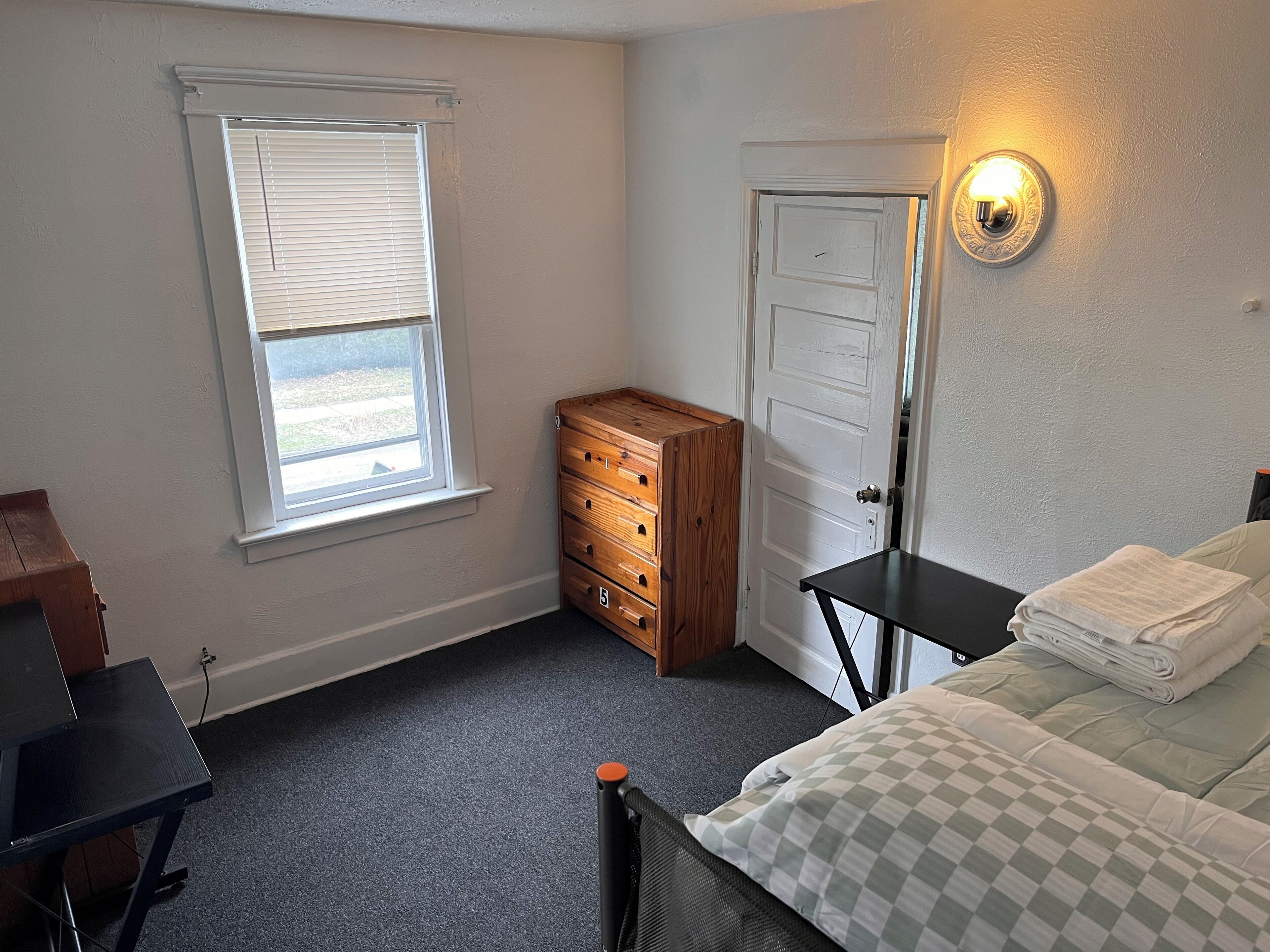 A bedroom with a bed, a dresser, a desk, a window, and a door.