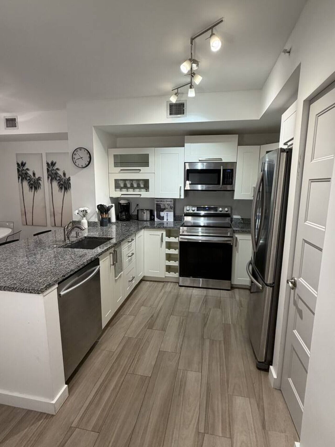 A modern kitchen with white cabinets, stainless steel appliances, a granite countertop, and a clock on the wall.