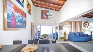 Un coin repas avec une table noire, des chaises et un plateau contenant des salières et des poivrières. On aperçoit également un canapé bleu et une décoration murale représentant un gouvernail de bateau en bois.