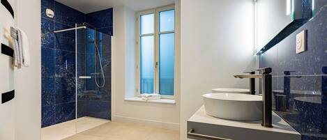 A modern bathroom with a glass-enclosed shower, a large window, and two sinks.