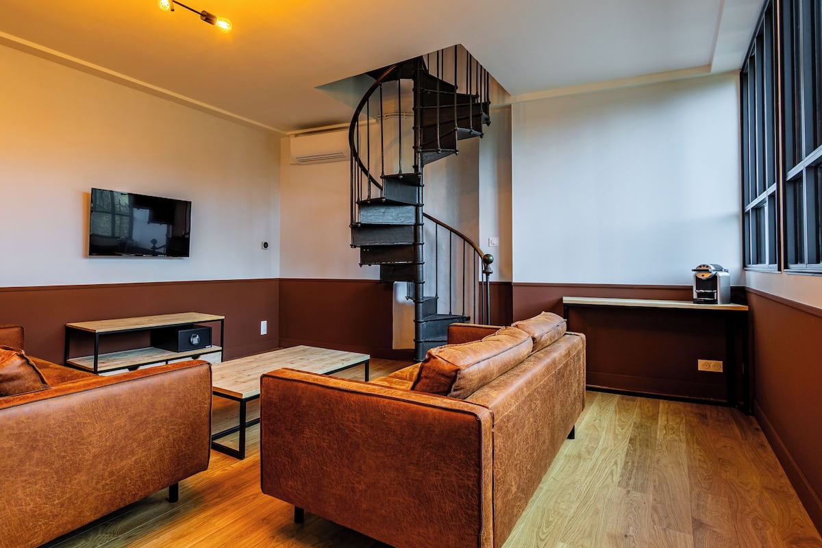 Ein modernes Wohnzimmer mit Wendeltreppe, Ledersofas, einem Flachbildfernseher und einer Kaffeemaschine.