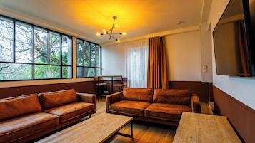 Una sala de estar moderna con sofás de cuero, una mesa de centro de madera y un comedor. Amplias ventanas ofrecen vistas a árboles al exterior.