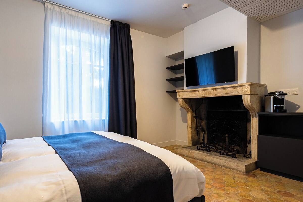 Ein Hotelzimmer mit Bett, Kamin, Fernseher und einem Fenster mit Vorhängen.