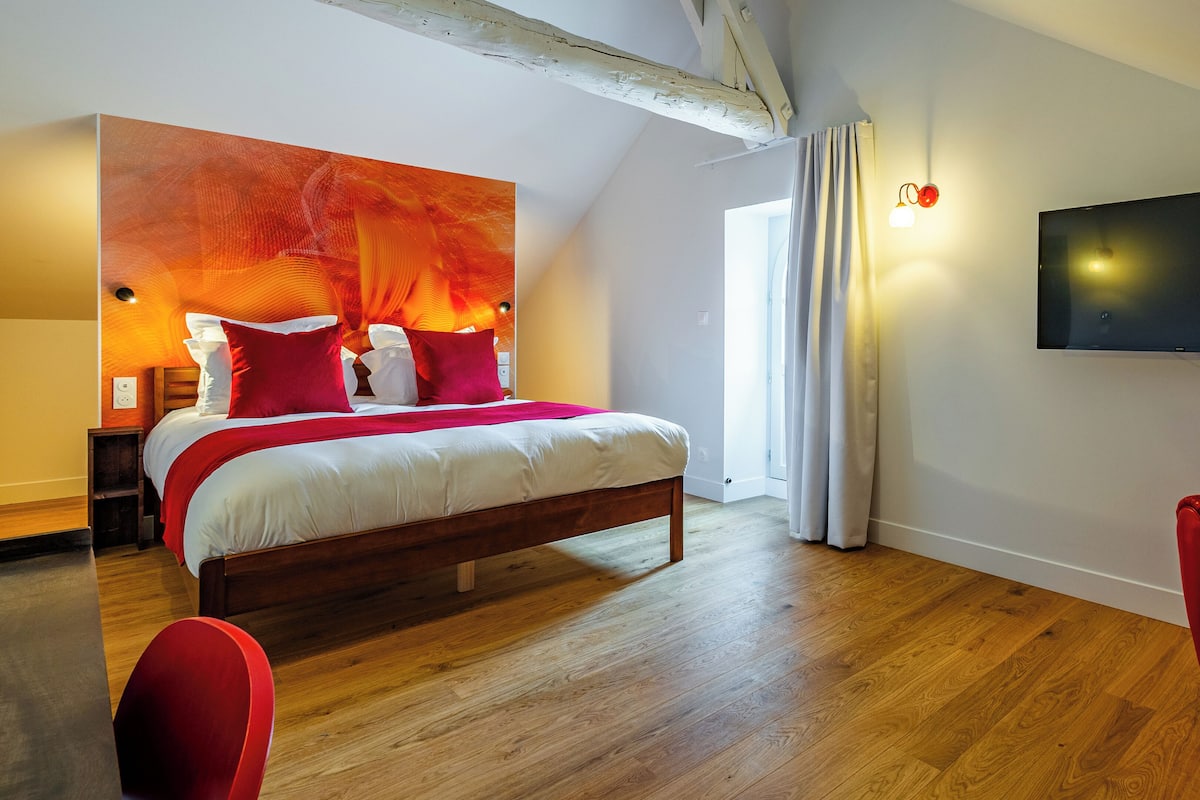 Ein modernes Schlafzimmer mit einem hölzernen Bett, roten Akzenten, einem Flachbildfernseher und einem roten Sessel.