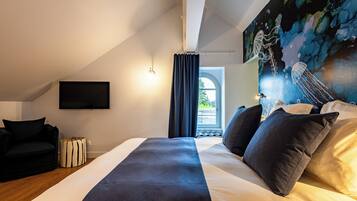 Quarto com cama, televisão, poltrona e um quadro na parede.