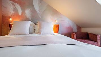 A bedroom with a large bed, two bedside lamps, a red armchair, and a wall with feather patterns.