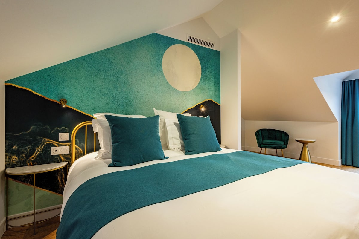Ein modernes Hotelzimmer mit einem großen Bett, einem Nachttisch, einem Sessel und einem runden Tisch.
