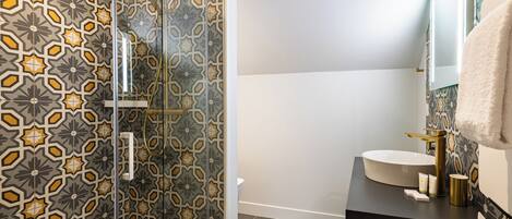 A bathroom with a patterned shower wall, a sink with a gold faucet, and a towel hanging on the wall.