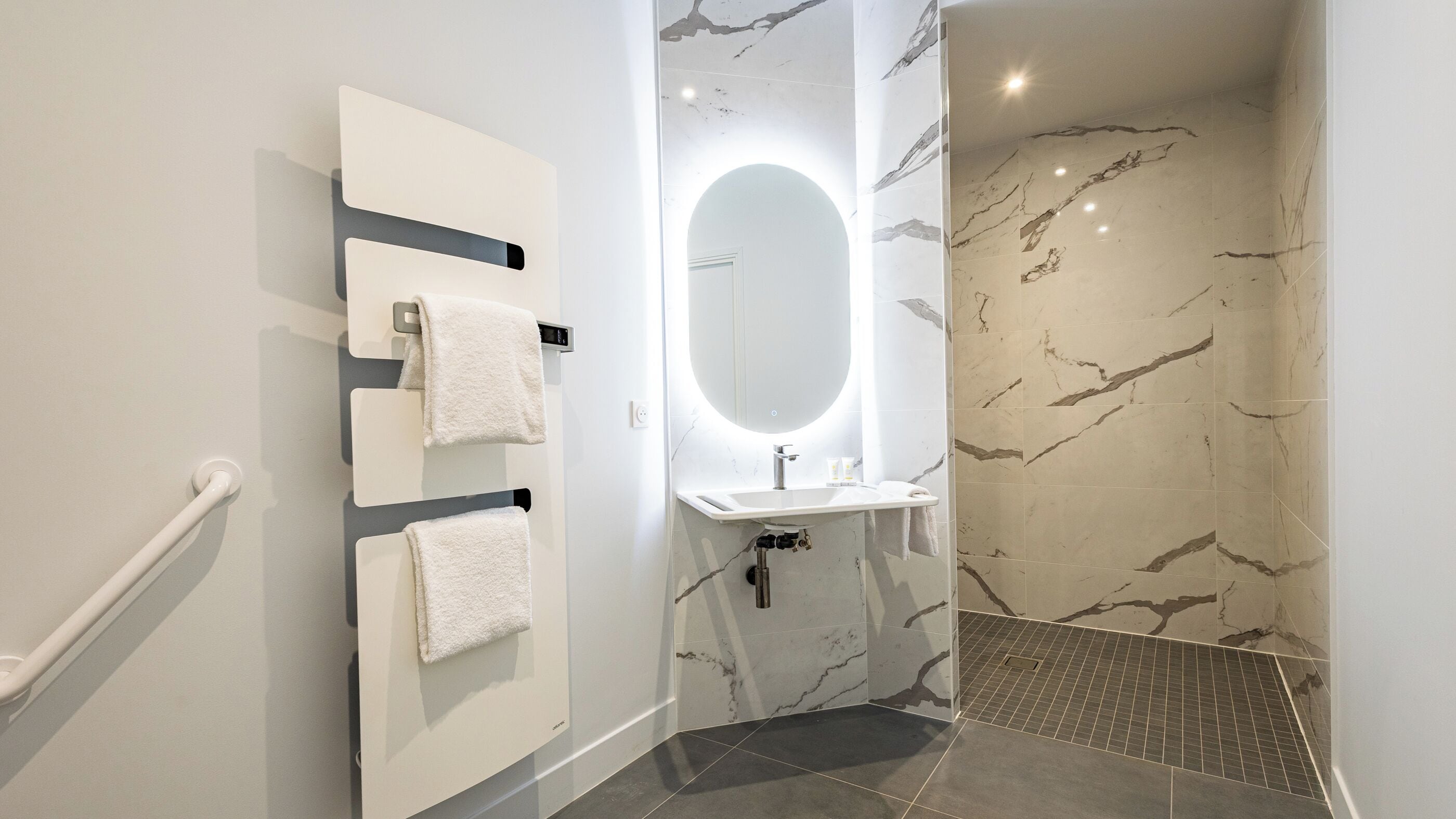 Une salle de bain moderne avec un meuble-lavabo blanc, un grand miroir et un espace douche aux carreaux de marbre.