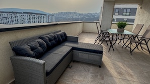 A rooftop terrace with a sectional sofa, a small table, and chairs.