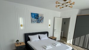 A modern bedroom with a large bed, bedside tables, a decorative light fixture, and a painting on the wall.
