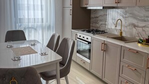 A modern kitchen with a dining area, featuring a marble countertop, stainless steel appliances, and a chandelier.