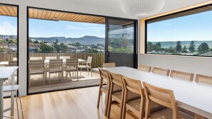 Un espace de restauration moderne avec une longue table et des chaises, de grandes fenêtres offrant une vue sur le paysage urbain et les montagnes, ainsi qu’un luminaire suspendu au plafond.