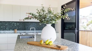 Un comptoir de cuisine sur lequel se trouve un vase blanc contenant des feuilles vertes et trois poires, une planche à découper en bois et un couteau.