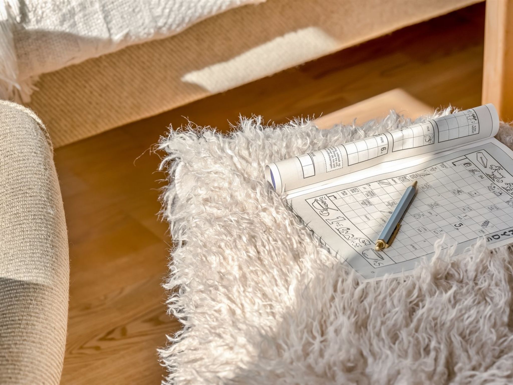 Una habitación acogedora con piso de madera, un tapete blanco mullido y una cama con manta blanca.