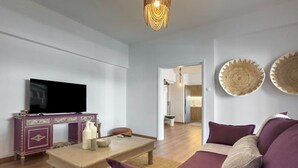 A living room with a television, a purple sofa, a wooden coffee table, and decorative woven wall hangings. - Phaedrus Living: Kallithea Heights Residence (Kallithea)
