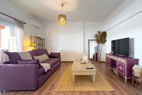 A modern living room with a purple sofa, a wooden coffee table, a TV, and a mirror. - Phaedrus Living: Kallithea Heights Residence (Kallithea)