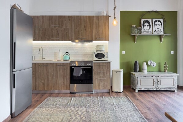 Una cocina moderna con armarios de madera, un refrigerador de acero inoxidable, horno empotrado y microondas. Hay una alfombra en el suelo y una lámpara colgante.